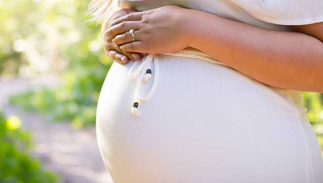 A pregnant belly with hands resting on the top in a light and bright outdoor setting