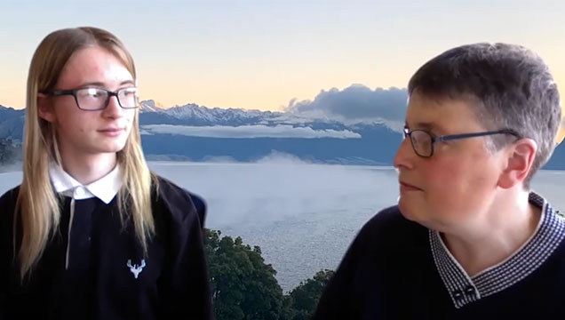 Dima looks to his mother, Anita, who is talking. They appear in front of a background of mountains and cloud cover.