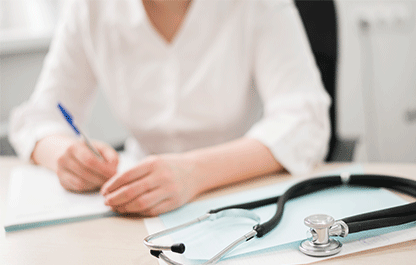 Doctor, face obscured, writing on a notepad with a stethoscope in view.