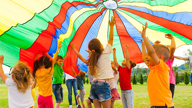 A group of young children play together under a large and colourful parachute.