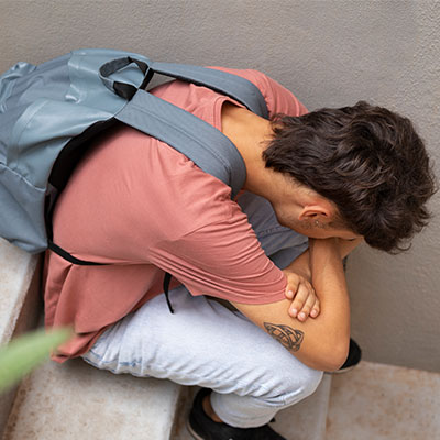 A young man sits on stairs and crouches over, looking at his arms