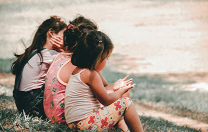 Children sitting outside on the grass next to one another in a row during the daytime.